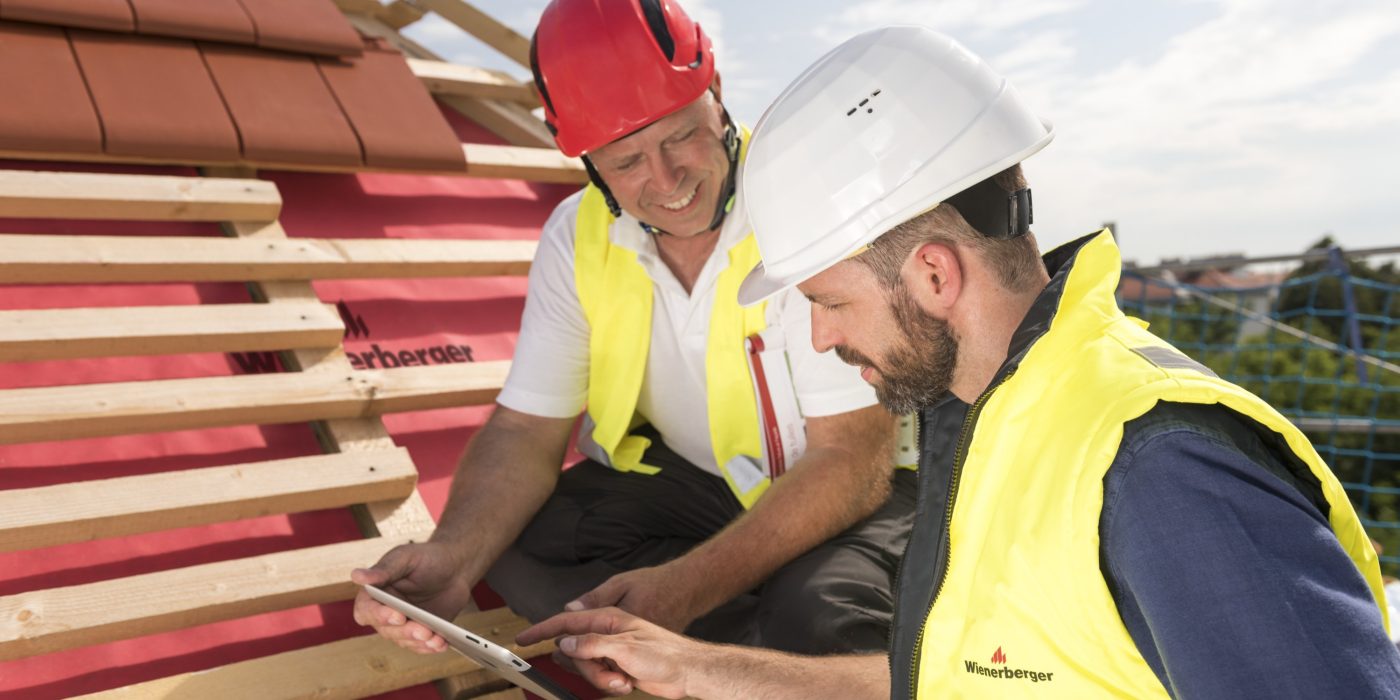 Urban roofer and product manager with tablet computer explaining product advantages to urban roofers wearing safety jackets and hard hats
