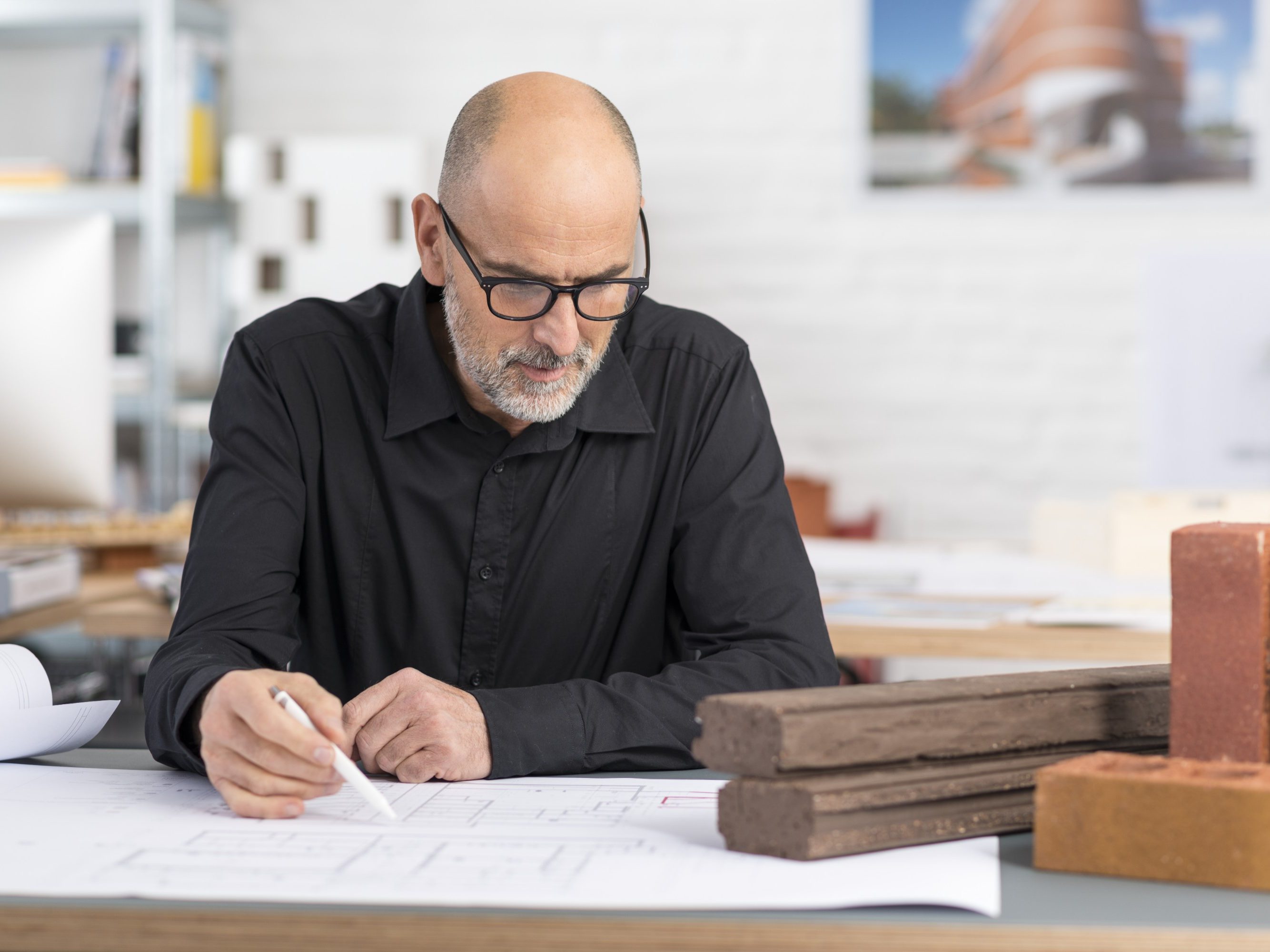 Senior architect sitting at office desk with blueprint and a selection of Wienerberger facing bricks