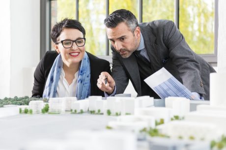 Man and woman talking about a new building project pointing at an architectural model