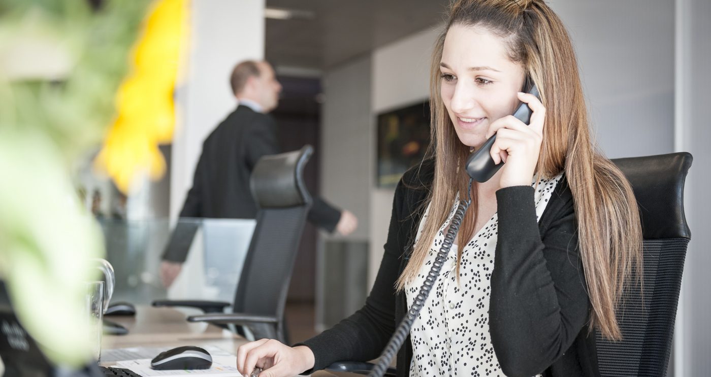 Young woman at reception desk holding telephone