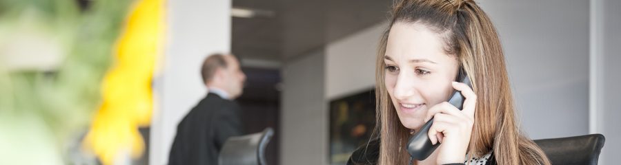 Young woman at reception desk holding telephone