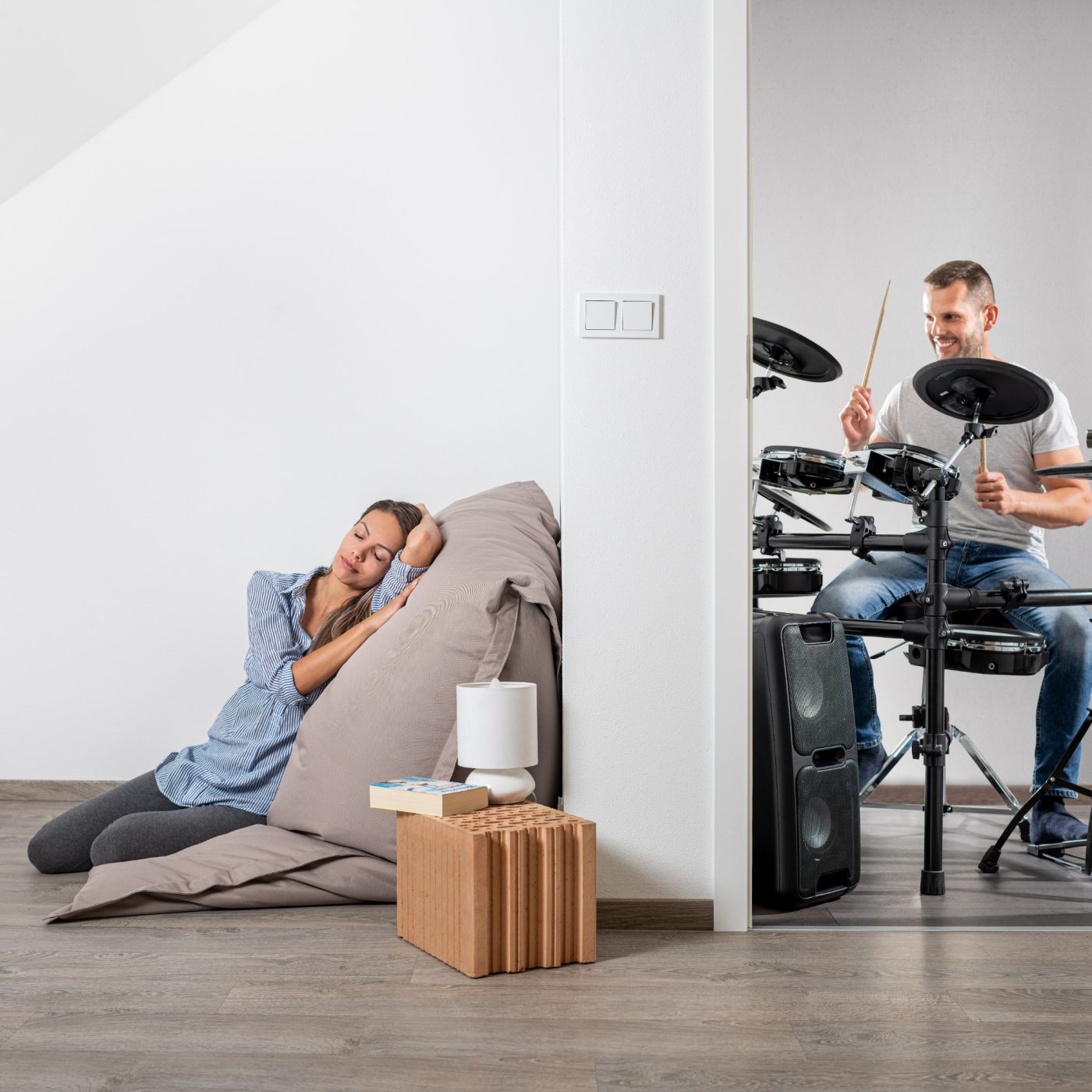 Muž hrající na bicí a v druhé místnosti klidně ležící žena cz