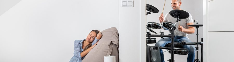 Muž hrající na bicí a v druhé místnosti klidně ležící žena
