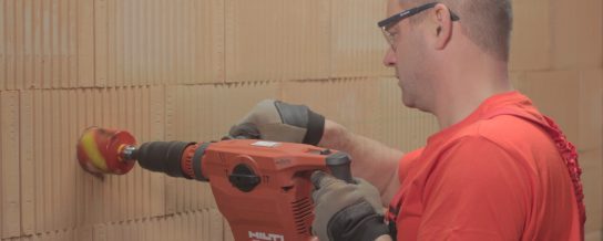 A man drilling holes for electrical boxes into a brick wall