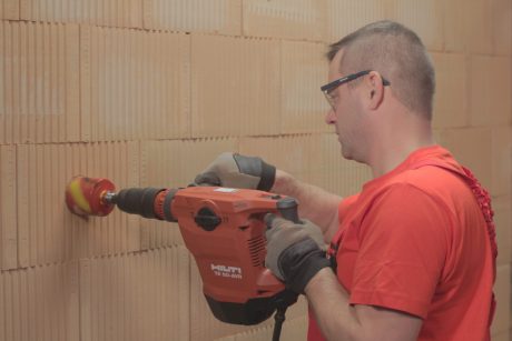 A man drilling holes for electrical boxes into a brick wall