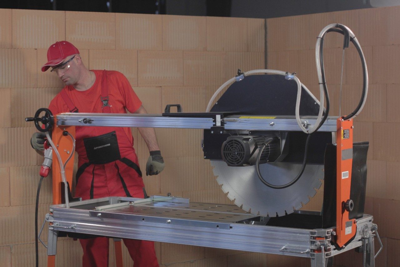 A man standing behind an electric saw for cutting bricks (cooled water)