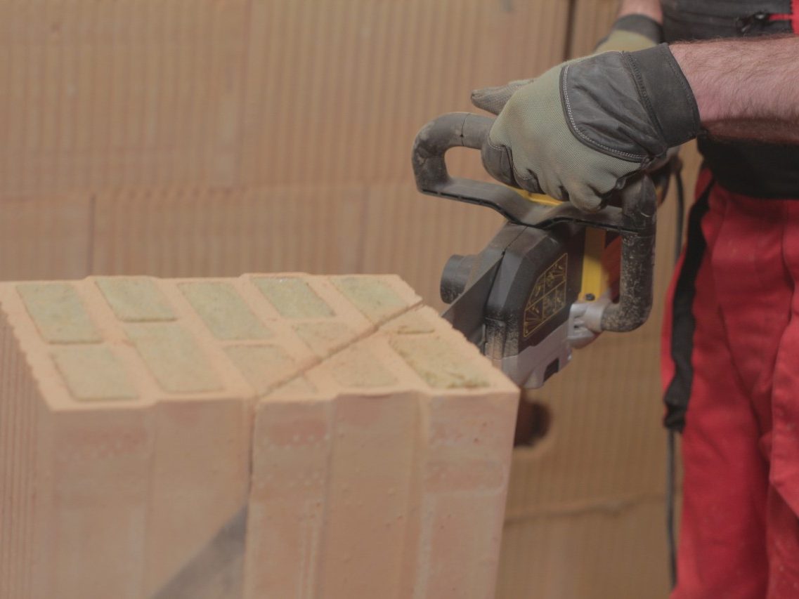 Male hands cutting with an electric saw brick Porotherm T Profi