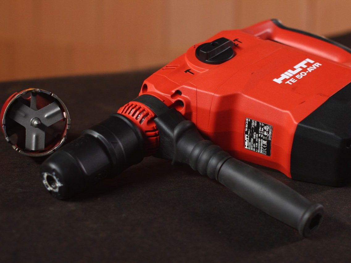 A drill with a drill bit on a black table in front of a brick wall