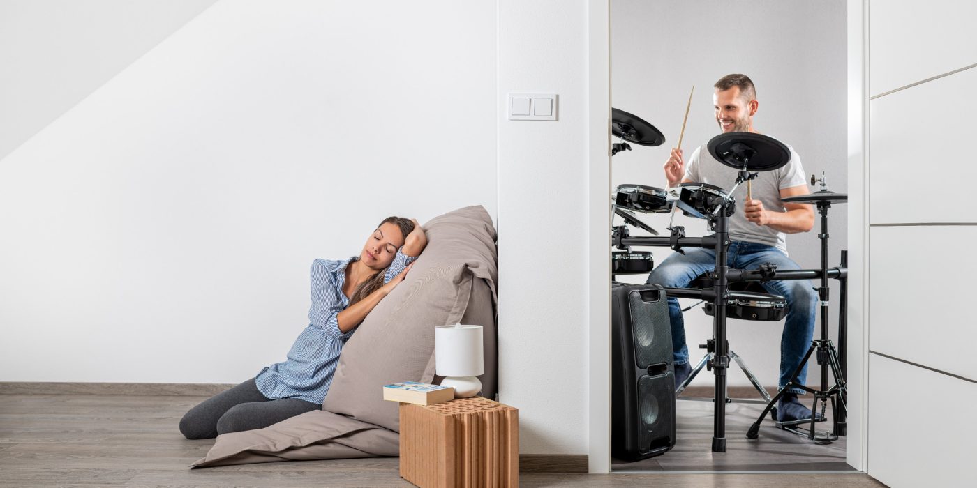 Muž hrající na bicí a v druhé místnosti klidně ležící žena cz