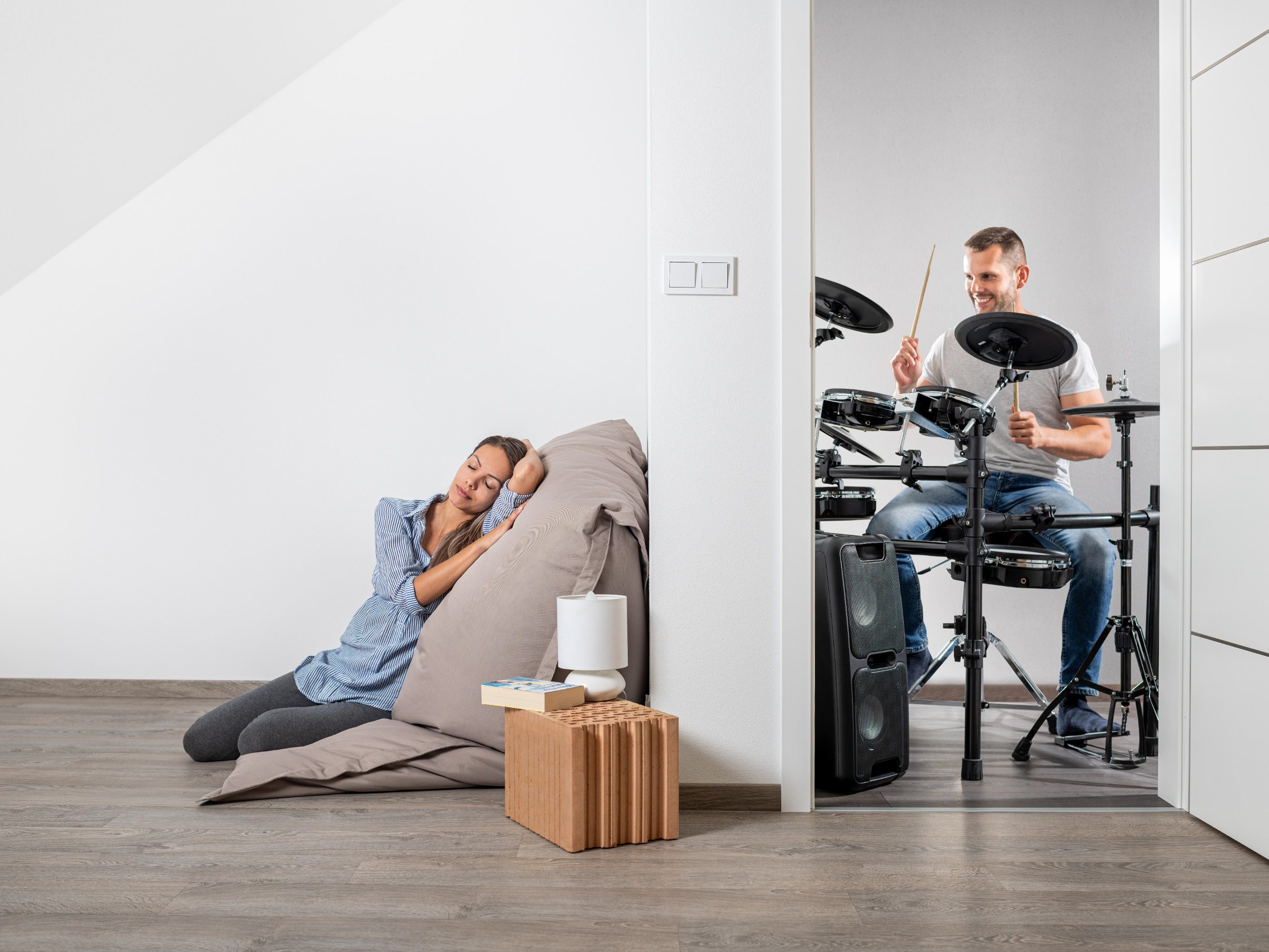 Muž hrající na bicí a v druhé místnosti klidně ležící žena cz